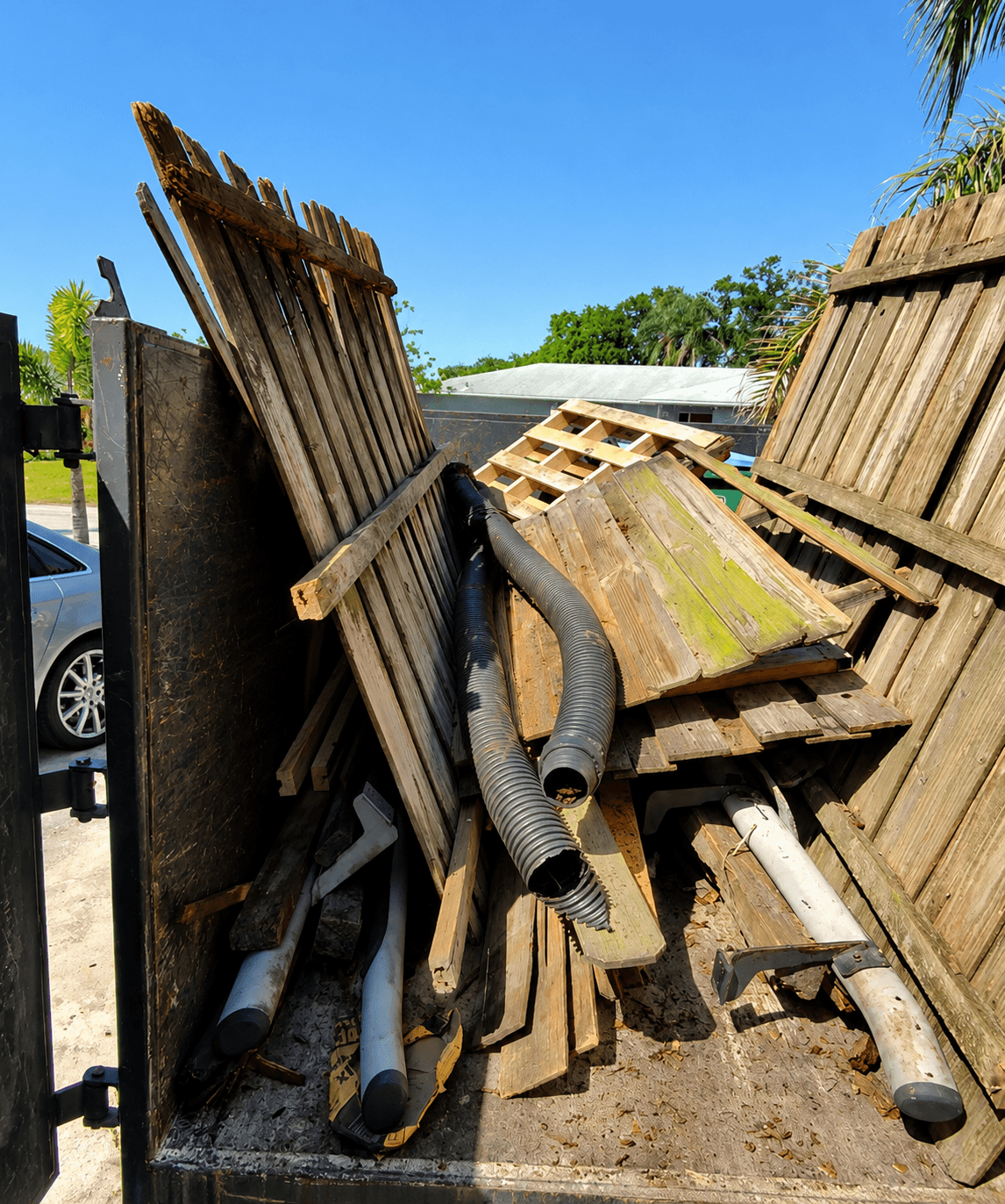 Weathered wooden fence panels and black drainage pipes piled inside a large metal dumpster.